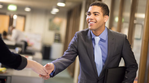 young man arrives at his interview , resume under his arm greeting his interviewer